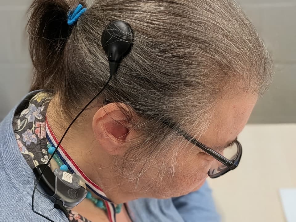 Bewoonster met een cochleair implantaat: de spoel zit op haar hoofd, de processor hangt aan een koord om haar hals.