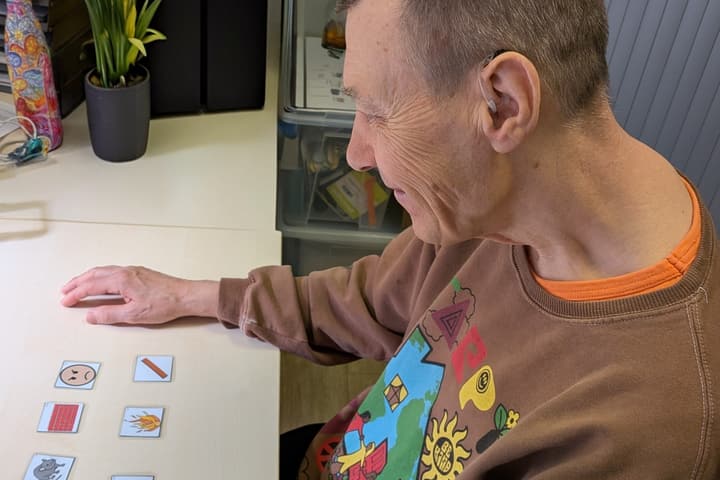 Bewoner met hoortoestel legt pictogramkaartjes op tafel.